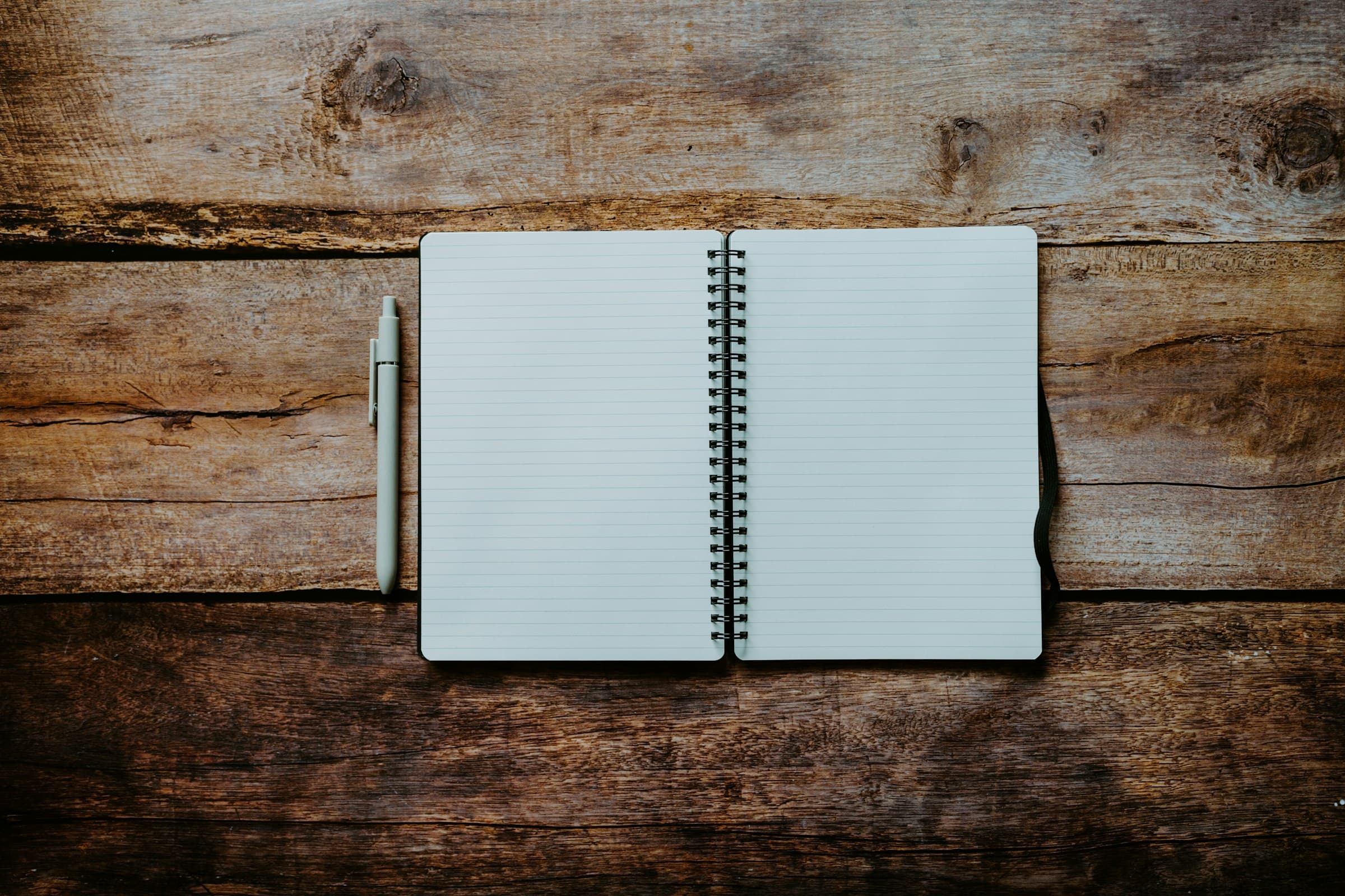 An open notebook with a pen resting on a wooden surface